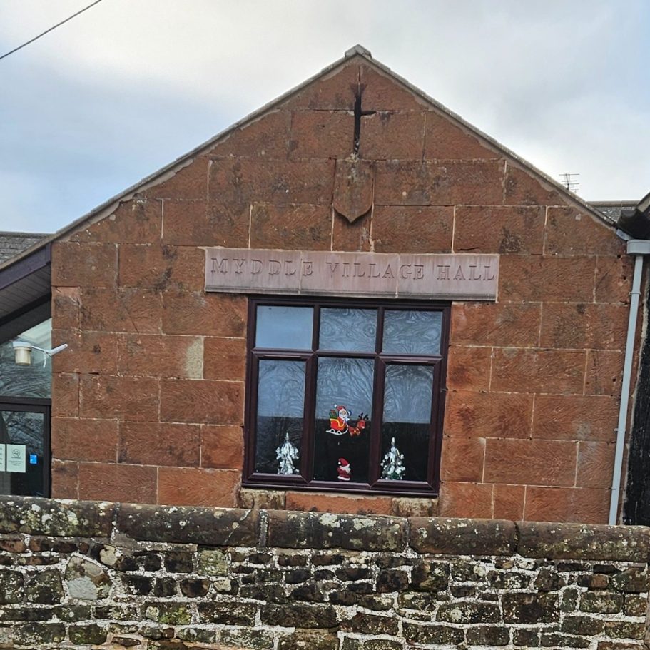 Stone wall building with a window displaying decorative flowers and religious symbols.