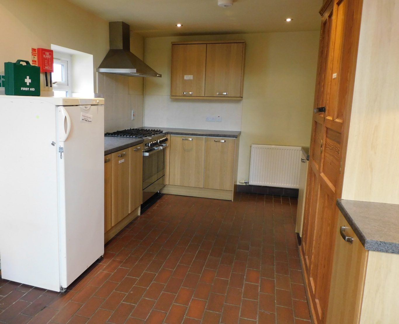 Kitchen area around the cooker A clean kitchen featuring wooden cabinets, a fridge, and stainless steel appliances.