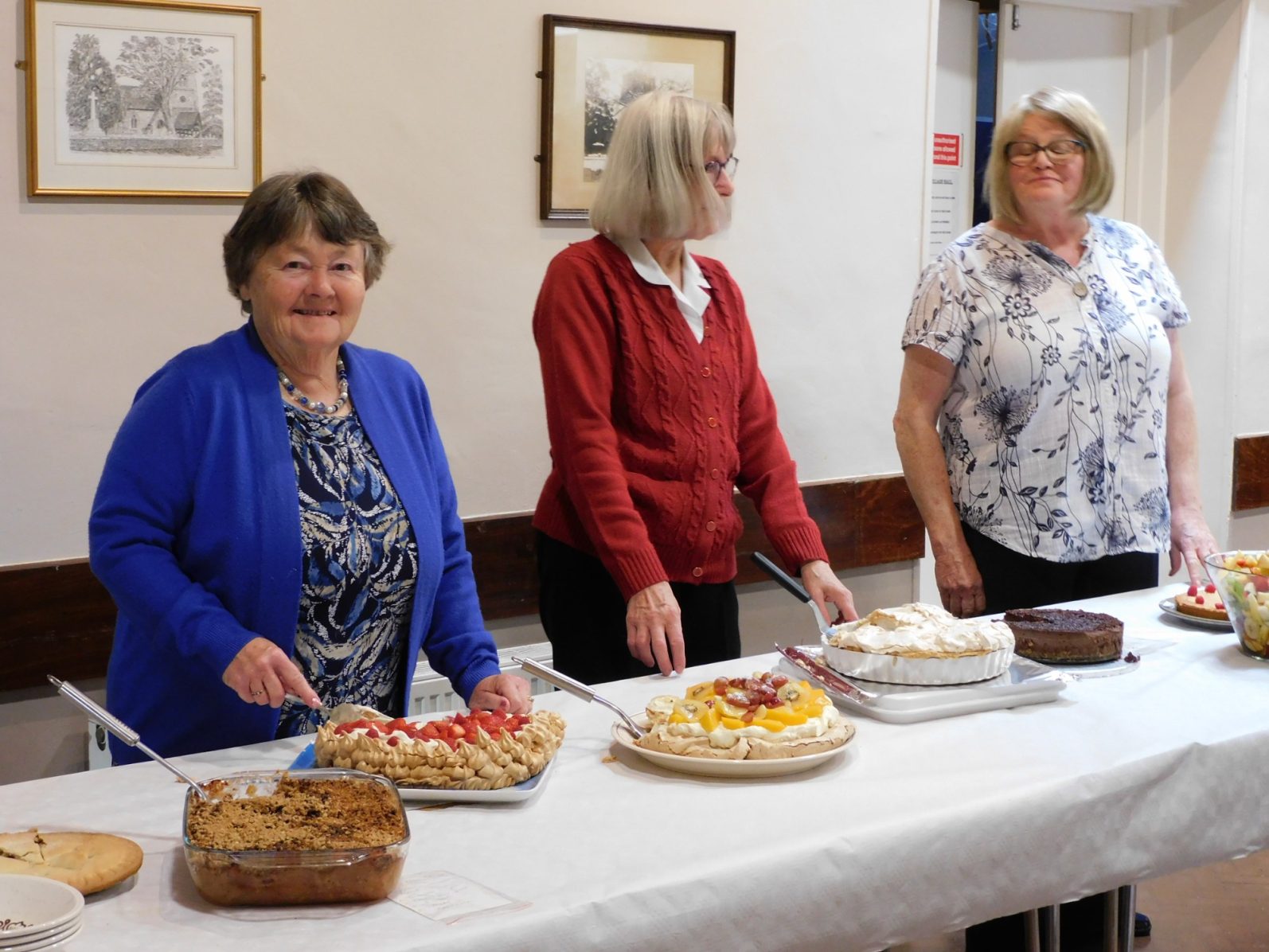 Desserts being served at the harvest lunch Three women stand behind a table displaying various cakes and desserts.